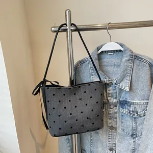 Detail van grijze bucket bag met zwarte stippen en een decoratief lint op het handvat