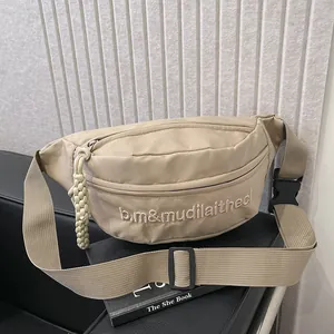Detail of beige nylon crossbody bag with embroidery and woven rope zipper pull