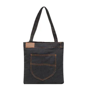 Denim tote bag with orange contrast stitching and brown leather label on white background