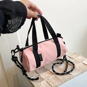 Detail of pink cylindrical oxford mini bag featuring black handles and woven rope strap