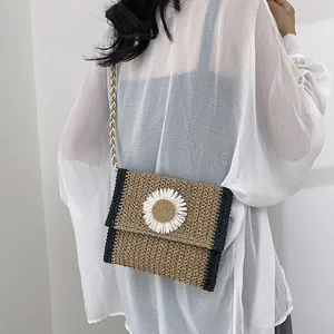 Detail of straw woven crossbody bag featuring white daisy flower and black trim