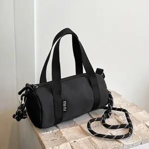 Detail of a mini black cylindrical crossbody bag with woven cord strap on stone stand