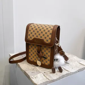 Detail of brown clover pattern crossbody bag with golden fashion text and plush charm
