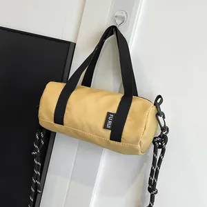 Close-up of yellow mini cylinder crossbody bag with black handles and woven rope strap
