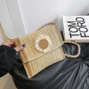 Close-up of handwoven straw crossbody bag featuring a daisy charm and envelope flap design