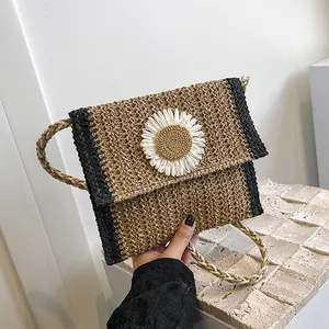 Detail of handwoven straw bag with white daisy decoration and a slim woven strap