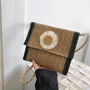 Close-up of handmade straw crossbody bag with white daisy flower detail and woven strap