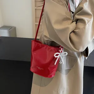 Detail of red glossy bucket bag featuring a pearl bow charm and metal heart pendant