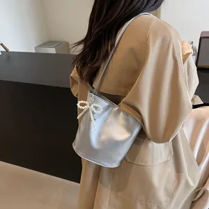 Detail of silver metallic bucket bag featuring a pearl bow charm and Fashion logo