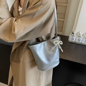 Close-up of a glossy silver bucket bag with pearl bow charm and embossed fashion text