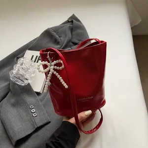 Detail of red bucket bag with pearl bow charm and polished finish on white bedding