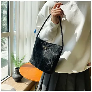 Détail d'un sac bandoulière noir plissé avec logo triangulaire sur une table en bois