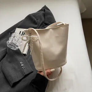 Close-up of cream bucket bag featuring pearl bow charm and minimalist logo detail