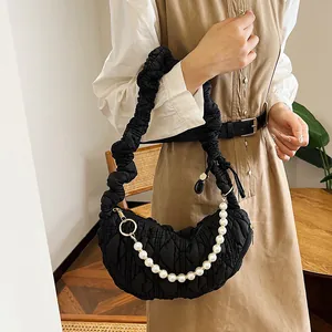 Close-up of black quilted cloud bag with pearl chain strap worn by a model indoors