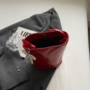 Glossy red bucket bag with pearl bow pendant and metallic magnetic closure detail