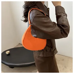 Detail of a bright orange faux crocodile texture crescent underarm bag on shoulder