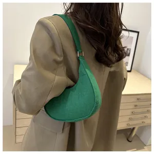 Detailed view of a green crocodile embossed hobo bag worn by a model in a minimalist room