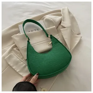 Detail of green hobo bag with crocodile texture and gold zipper on a beige background