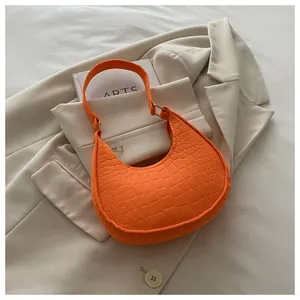 Detail of orange faux crocodile skin texture on shoulder bag over a beige blazer