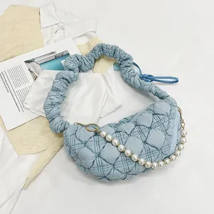 Detail of light blue quilted baguette bag featuring a pearl chain and ruched shoulder strap