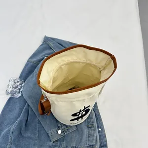 Canvas bucket bag with brown leather trim and dollar sign print for casual styling