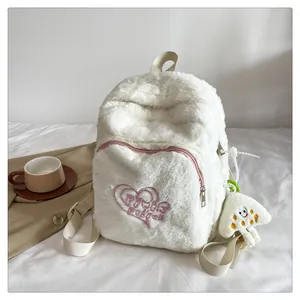 Close-up of plush white backpack featuring pink heart embroidery and a fuzzy charm