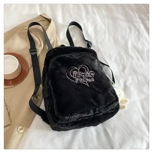 Close-up of black plush backpack with pink heart embroidery and cute white doll pendant