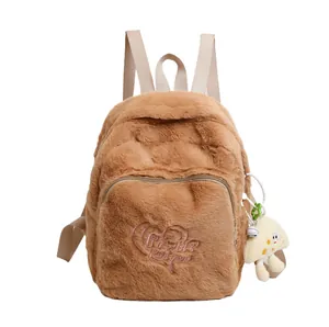 Brown plush backpack with heart embroidery and a small cartoon doll charm on white background