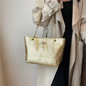 Detail of gold crocodile texture tote bag with metallic deer charm and chain strap