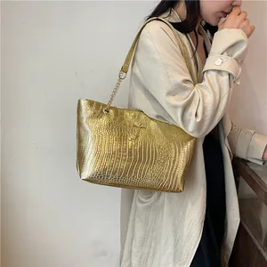 Detail of a bright gold tote bag with crocodile pattern and metal deer pendant