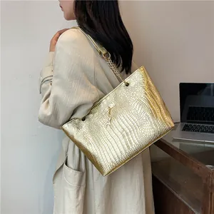 Detail of gold tote bag featuring crocodile pattern texture and metallic chain strap