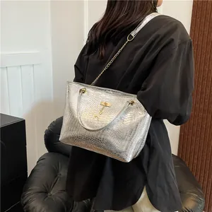 Detail of silver crocodile-embossed tote bag with golden chain strap and deer pendant