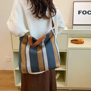 Détail d'un grand cabas en toile rayée avec poignées marron porté par un mannequin
