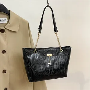 Detail of black crocodile-embossed tote bag with golden metal buckle and deer pendant