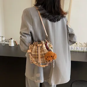 Detail of plaid wool bucket bag with teddy charm shown as a crossbody on a grey suit