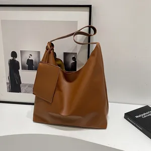 Close-up of a large brown leather tote bag with wide strap and matching mini pouch