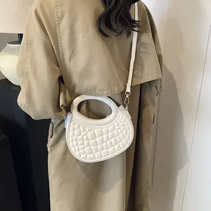 Detailed close-up of textured moon-shaped bag in cream white on a model's trench coat