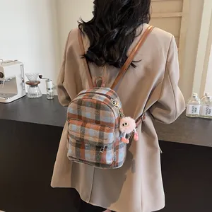 Detail of a vintage plaid wool backpack with brown leather straps and a plush charm