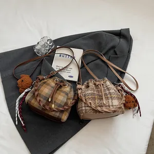 Detail of plaid wool bucket bags with leather base and teddy bear charm on grey coat