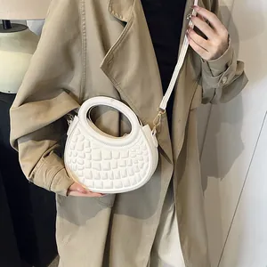 Close-up of white croc-embossed crescent bag with gold hardware on a trench coat model
