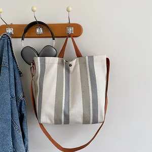 Détail d'un sac cabas en toile à rayures avec anses brunes et fermeture magnétique au mur