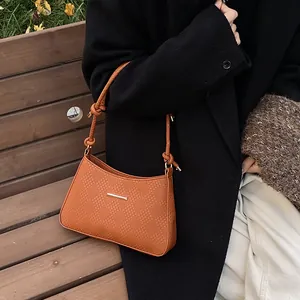 Close-up of caramel woven leather shoulder bag with a gold buckle on a model