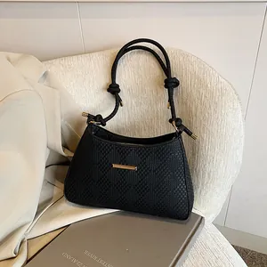 Close-up of black woven texture shoulder bag with gold hardware on a beige chair