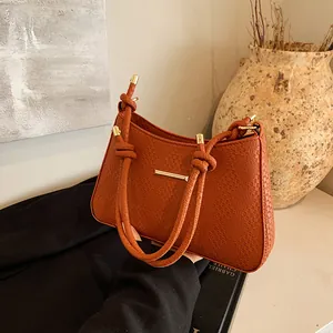 Detail of red-brown woven shoulder bag with gold metal trim and unique knot strap