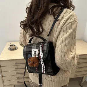 Dettaglio dello zaino a quadri con patch orsetto e ciondolo in peluche su maglione