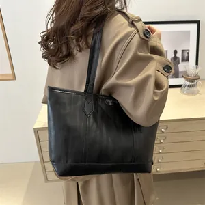 Detail view of black faux leather tote bag with vertical stripes and side brand tag