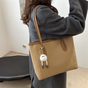 Dettaglio della borsa tote in pelle kaki con cuciture a contrasto e ciondolo mostro di peluche