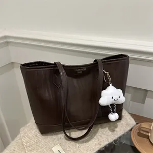 Detail of dark coffee textured leather tote bag with cloud charm on white knit