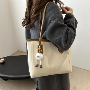 Dettaglio della borsa tote crema con finiture in pelle marrone e ciondolo di peluche