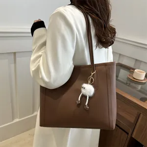 Dettaglio di una borsa tote marrone in pelle con un simpatico ciondolo in peluche bianco